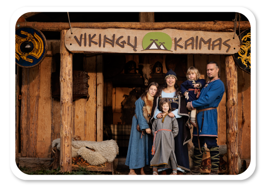 Vikingų kaimas. Penkių asmenų šeima stovi prie įėjimo į kaimą. Apsirengę tradiciniais drabužiais.